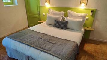 A neatly made bed with a grey and white duvet, two bedside tables with lamps, a green door, and a small window.