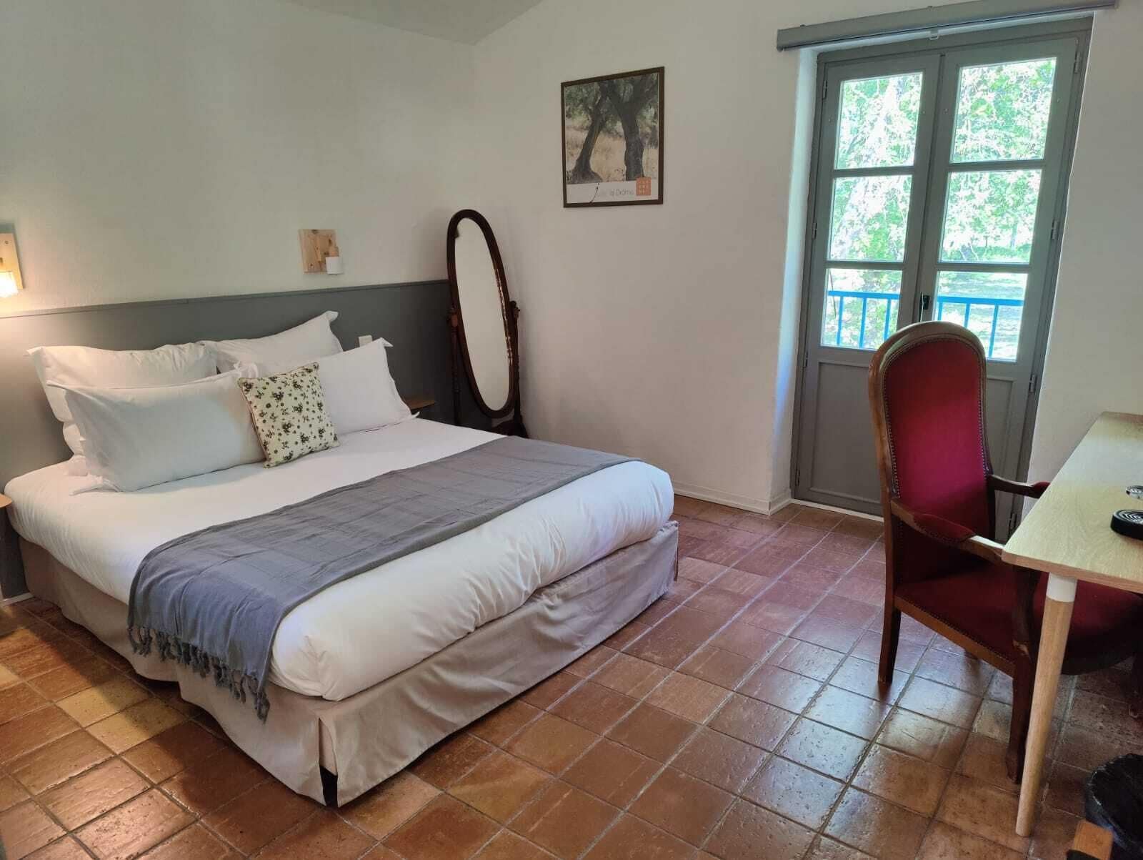 Un dormitorio ordenado con cama, una silla, una mesa y ventana con vista a la vegetación.