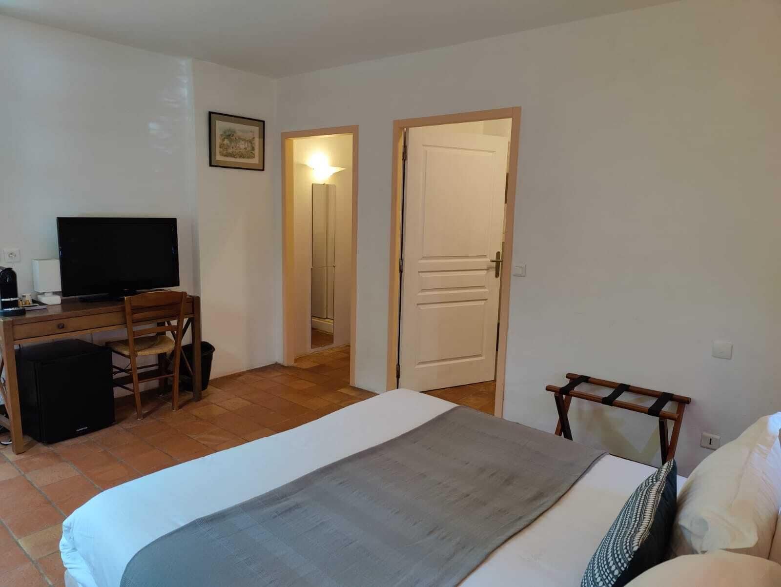 Habitación de hotel con cama, escritorio con computadora, silla, televisión y puerta que da a otra habitación.