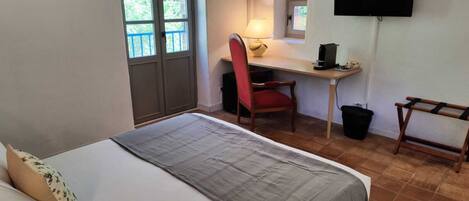 A bedroom with a bed, a desk, a chair, a television, and a window.