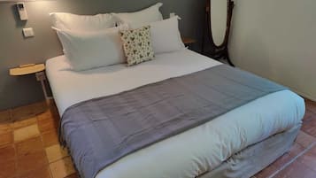 Uma cama bem arrumada com roupa de cama branca e cinza, uma cabeceira de madeira e uma mesa de cabeceira com uma luminária.