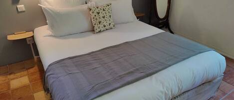 A neatly made bed with white and gray bedding, a wooden headboard, and a nightstand with a lamp.