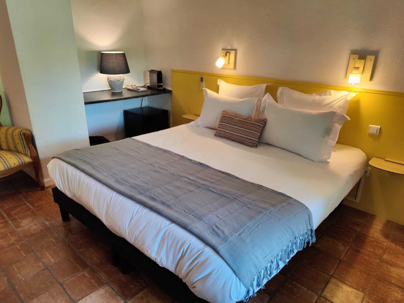A neatly made bed with a grey blanket, a bedside table with a lamp, and a chair.