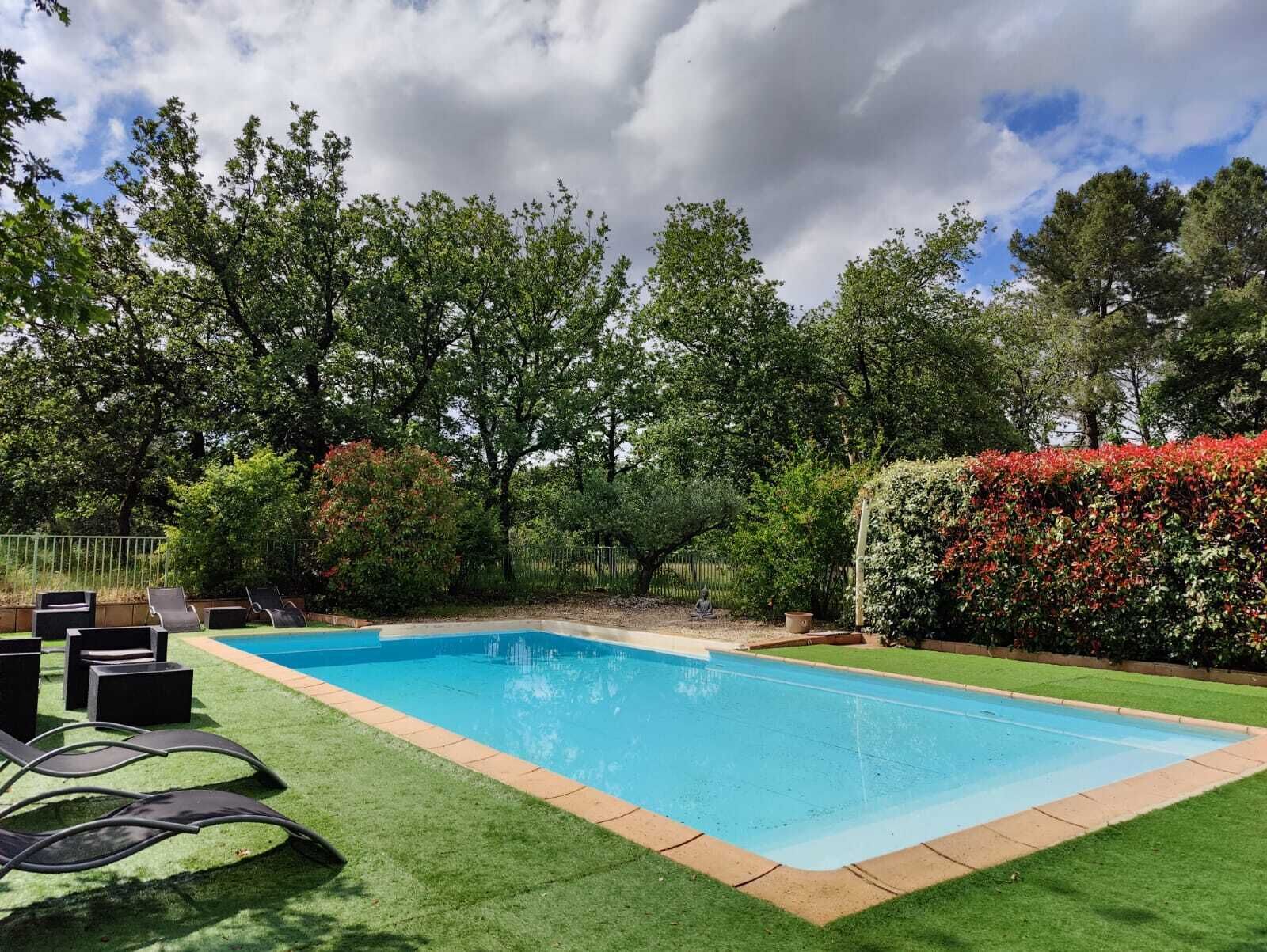 A rectangular swimming pool with a surrounding grassy area and a few lounge chairs.