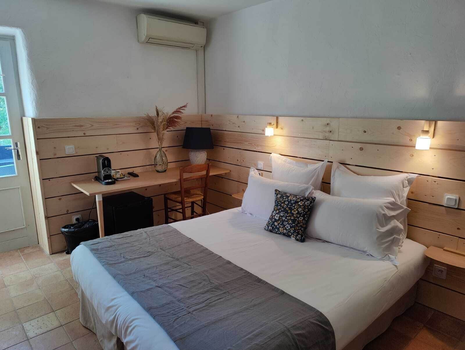 Een slaapkamer met een bed, nachtkastje, lamp en een klein bureau met stoel.