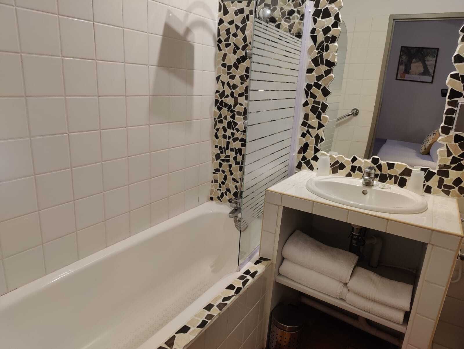 A bathroom with a white bathtub, a sink with a mosaic backsplash, and a mirror above the sink.