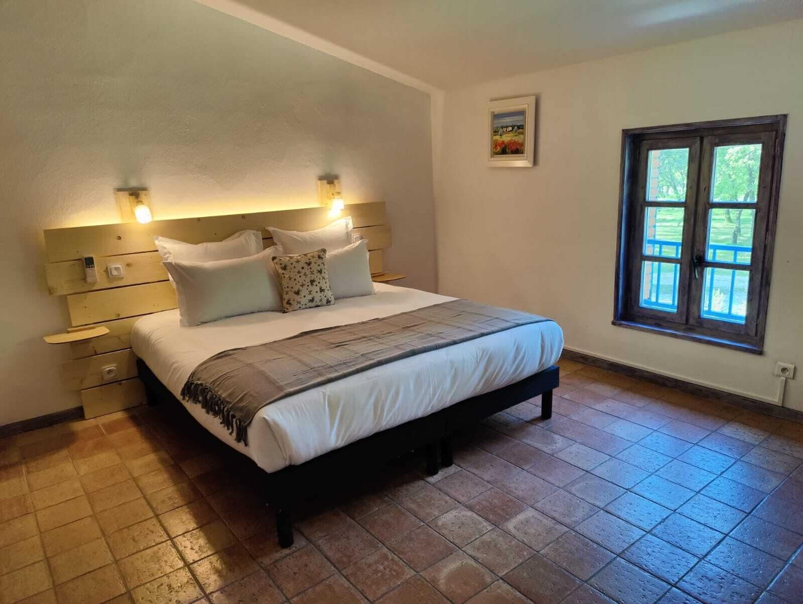 A bedroom with a bed, bedside tables, a window, and a wall-mounted picture.