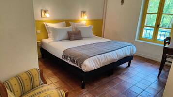 Un dormitorio con cama, mesitas de noche, una silla y ventana con vista a la vegetación.
