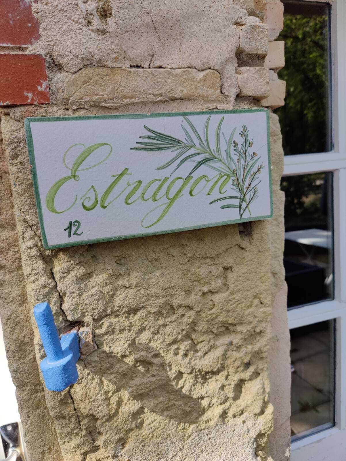 Une enseigne portant le nom «Estragon» et le numéro 12, fixée à un mur texturé, avec un objet en plastique bleu à proximité.