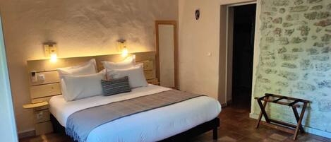 Un dormitorio con cama, mesitas de noche, un taburete de madera y una puerta que da a otra habitación.