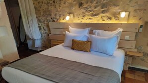 Una cama con ropa blanca, un plaid gris y un cabecero de madera con dos luces fijadas a la pared.