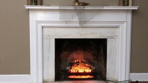A fireplace with a burning fire, a painting above it, and decorative bottles on the mantel.