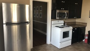 A kitchen with a stainless steel refrigerator, a white stove, black cabinets, and a microwave.