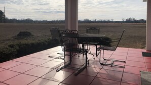 A covered patio with a table and chairs, a view of a field, and a cloudy sky.