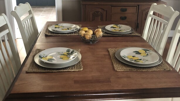 A dining table set with plates, a bowl of lemons, and a wooden cabinet with glass doors in the background.