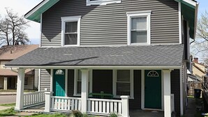 Ein zweistöckiges Haus mit Veranda, einer grünen Tür und einem kleinen Vorgarten.