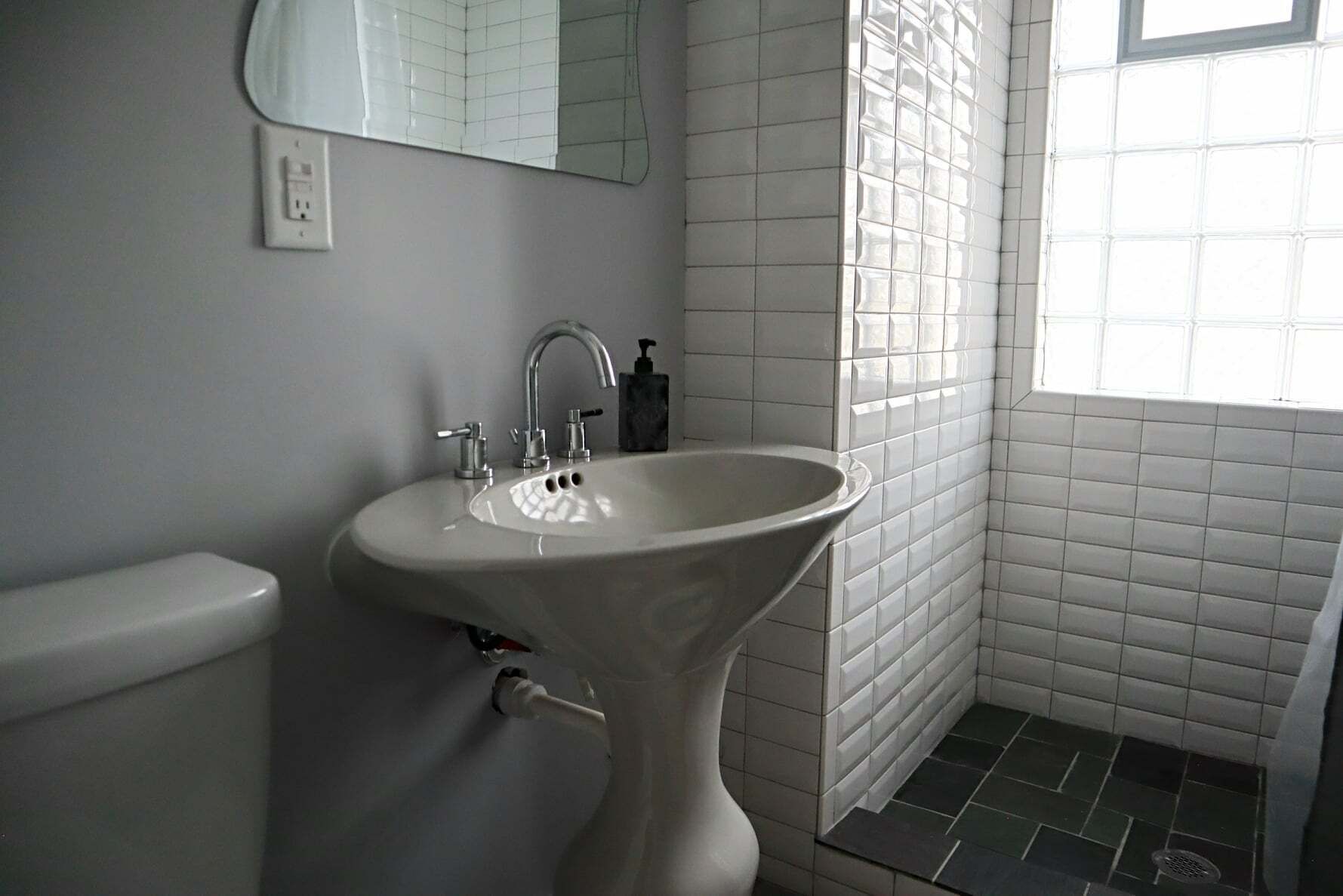 A bathroom with a pedestal sink, a toilet, a mirror, and a window.