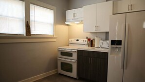 Eine kleine Küche mit weißen Geräten, darunter ein Herd, ein Backofen und ein Kühlschrank, sowie ein Fenster mit Jalousien.