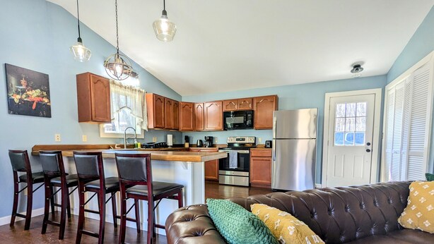 A modern kitchen with wooden cabinets, stainless steel appliances, and a bar area with stools. - Country Mama's Modern Artsy Cottage  (Sedgwick)