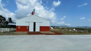 A single-story building with a red and white facade, a flag on top, and a clear sky in the background. - Cabaña tipo granero Granglam Ixkapada  (Ixtapan de la Sal)