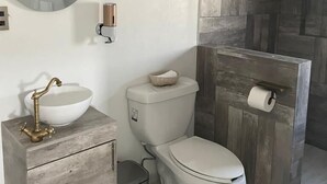 A modern bathroom with a wooden vanity, a round mirror, a toilet, and a shower area. - Cabaña tipo granero Granglam Ixkapada  (Ixtapan de la Sal)