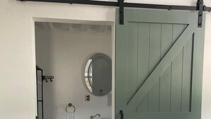 A room with a sliding barn-style door, a round mirror, a white sink, and a small wooden cabinet. - Cabaña tipo granero Granglam Ixkapada  (Ixtapan de la Sal)