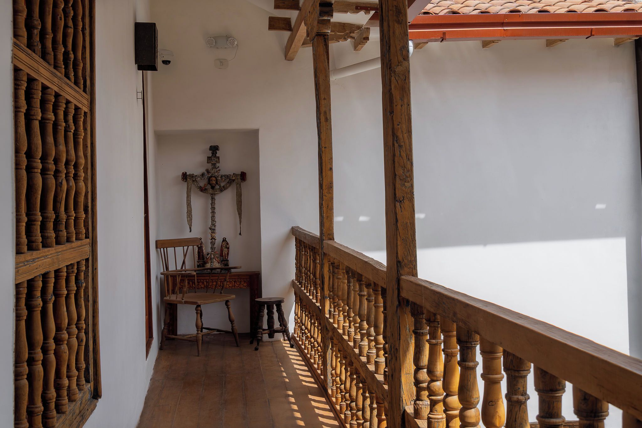 Una escalera de madera con barandillas, una silla de madera y una mesa con un crucifijo al fondo.