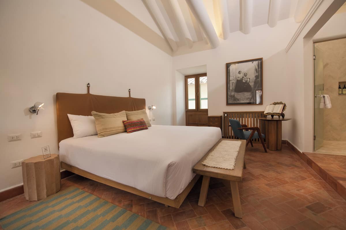 Un dormitorio con cama, mesita de noche, silla y una pequeña mesa con lámpara.