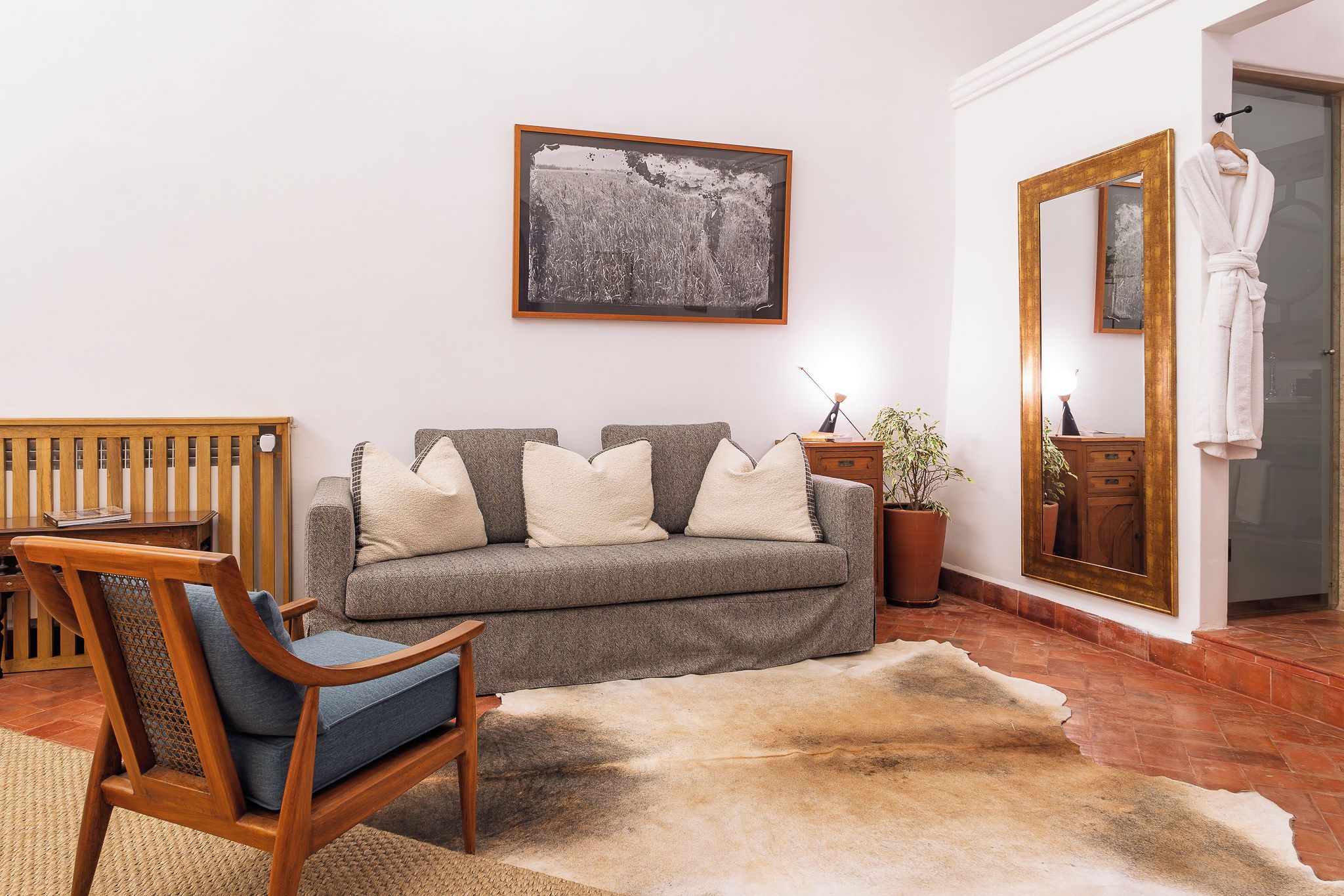 Ein Wohnzimmer mit einer Couch, einem Holzstuhl, einem Teppich, einer Topfpflanze und einem Spiegel.