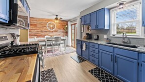 A modern kitchen with blue cabinets, a wooden dining table, and a brick accent wall.