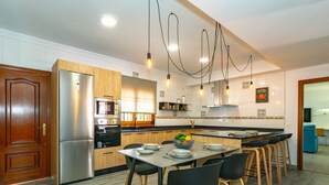 Une cuisine moderne avec des meubles en bois, des appareils en acier inoxydable, une table à manger avec des chaises et des luminaires suspendus.