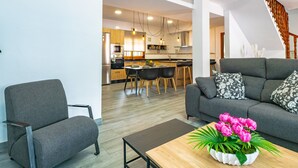 Un salon moderne avec un canapé gris, une table basse en bois et un coin repas, la cuisine étant visible au fond.