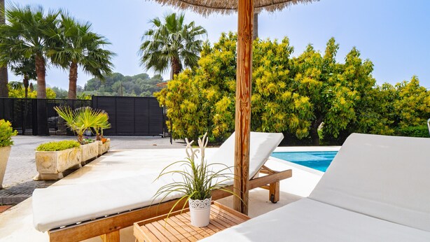 Un espace aménagé au bord de la piscine, avec des chaises longues, une table en bois et un parasol en chaume.