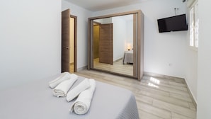 Une chambre à coucher avec un lit, un grand miroir, un téléviseur fixé au mur et une porte en bois.