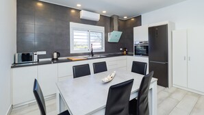 Une cuisine moderne avec un coin repas, dotée d’une grande fenêtre, d’appareils électroménagers intégrés et d’un design épuré et minimaliste.
