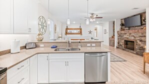 A modern kitchen with white cabinets, a central island, stainless steel appliances, pendant lighting, and a stone fireplace. - 🌴 Family Beach Retreat, Movie Theater, Game Room, Hot Tub, Near Ocean (Palm Coast)
