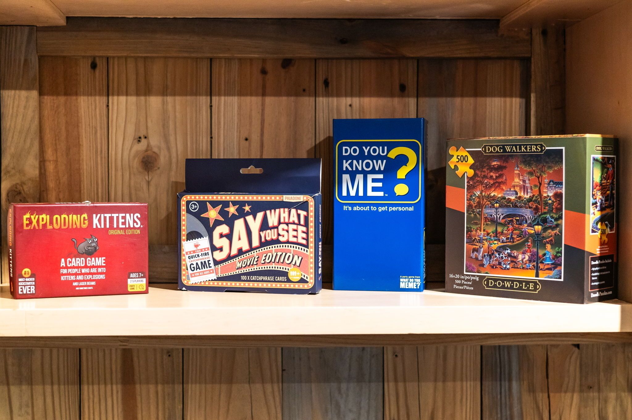 Una estanteria amb quatre jocs de taula: 'Exploding Kittens', 'Say What You See', 'Do You Know Me?' i 'Dog Walkers'.