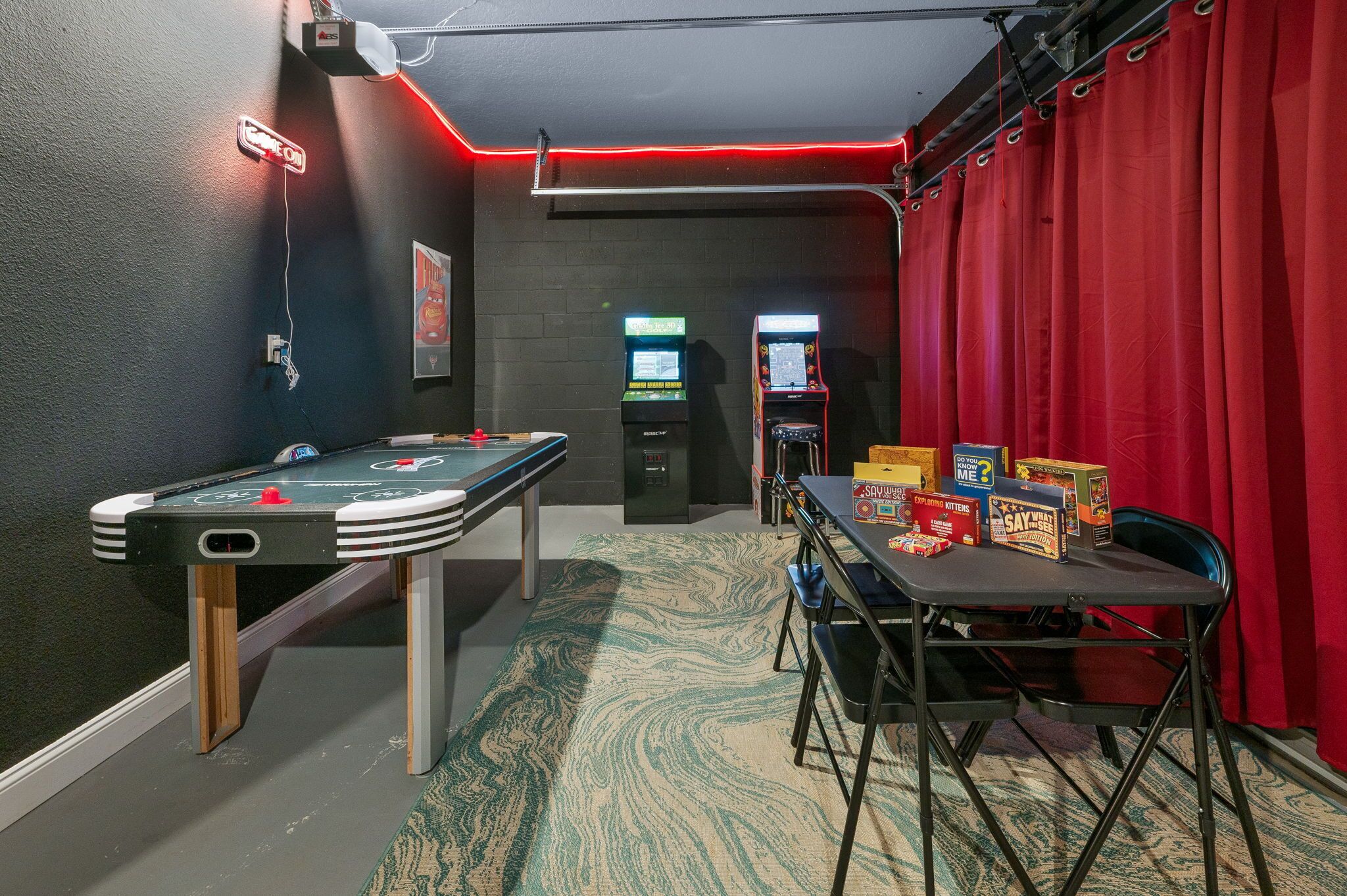 A pool table with a green felt surface, a red curtain, and arcade machines in the background.