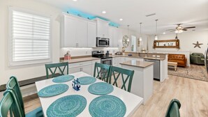 A modern kitchen with white cabinets, a central island, and a dining area with a white table and teal placemats. - 🌴 Family Beach Retreat, Movie Theater, Game Room, Hot Tub, Near Ocean (Palm Coast)