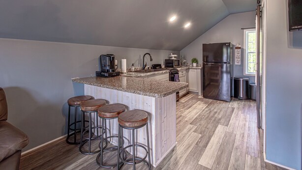 A kitchen with a bar area, wooden stools, a refrigerator, and a microwave.