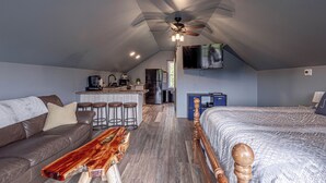 A spacious loft with a high ceiling, a kitchenette, a large bed, a wooden bench, and a ceiling fan.