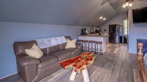 A modern living room with a brown leather sofa, a wooden coffee table, and a kitchen area in the background.
