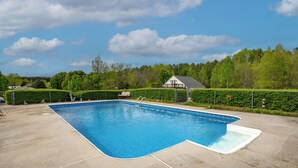 A rectangular swimming pool with a diving board, surrounded by a fence and a hedge.