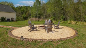 A circular outdoor seating area with a fire pit, surrounded by a gravel border and wooden chairs.