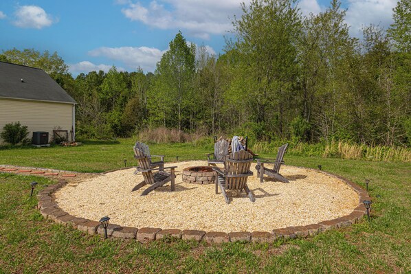 A circular outdoor seating area with a fire pit, surrounded by a gravel border and wooden chairs.