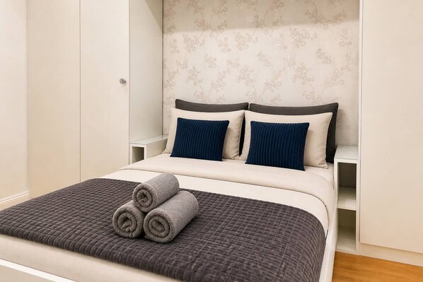 A neatly made bed with a quilted cover, two pillows, and rolled towels on a headboard with a floral pattern.