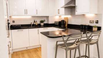 A modern kitchen with white cabinets, a black countertop, and two bar stools.
