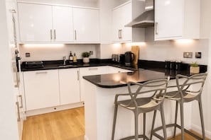 A modern kitchen with white cabinets, a black countertop, and two bar stools.