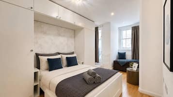 A modern bedroom with a large bed, built-in wardrobe, and a small seating area.