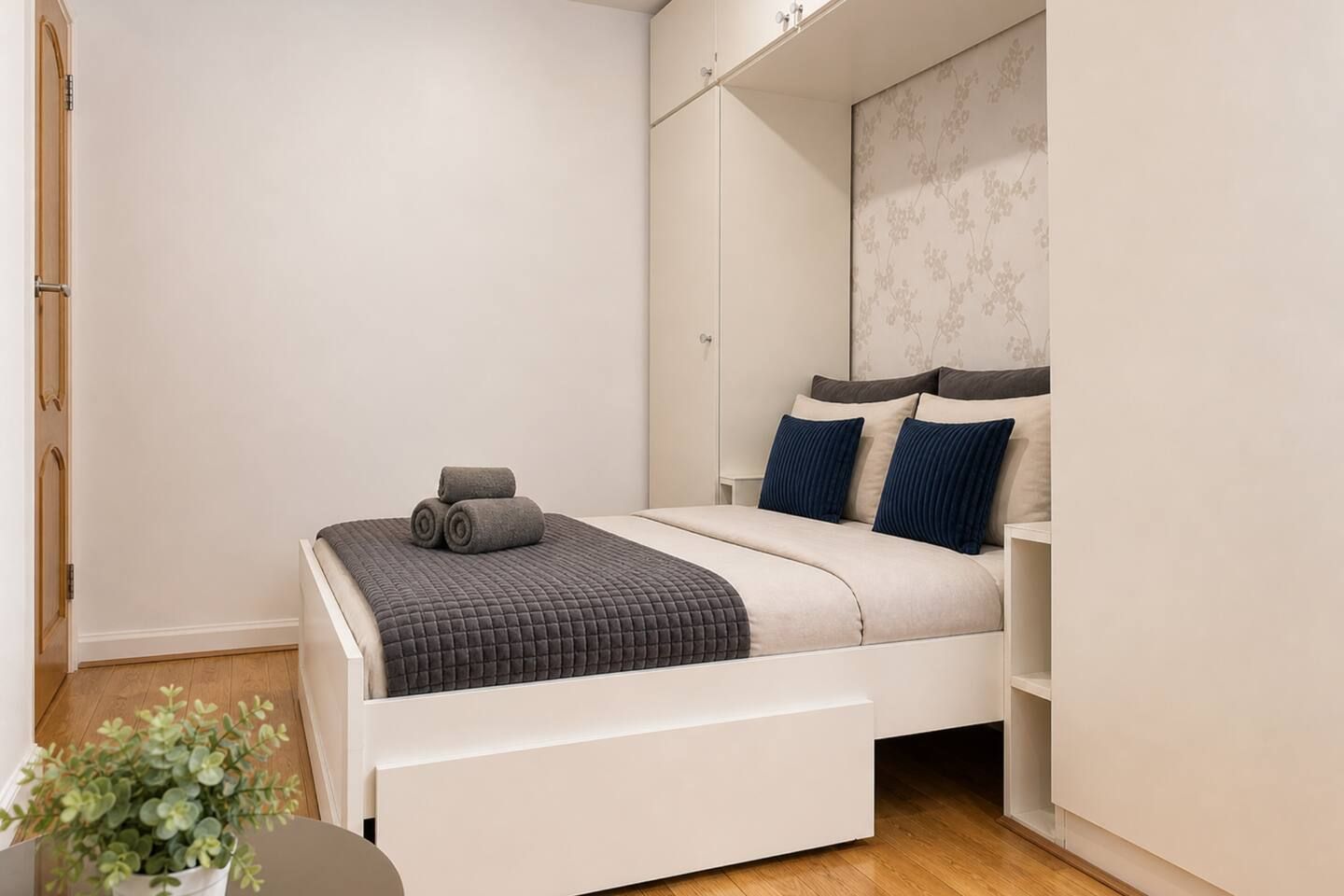 A bedroom with a bed, a nightstand, a potted plant, and a wardrobe.
